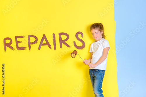 a little girl with a roller for painting in her hands  stands near a painted wall  wrote an inscription on the wall repair  choosing a color for repair