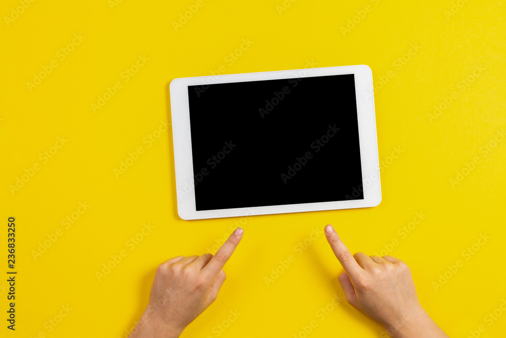 Kid hands finger pointing to tablet computer on yellow background Kid hands finger pointing to tablet computer on yellow background
