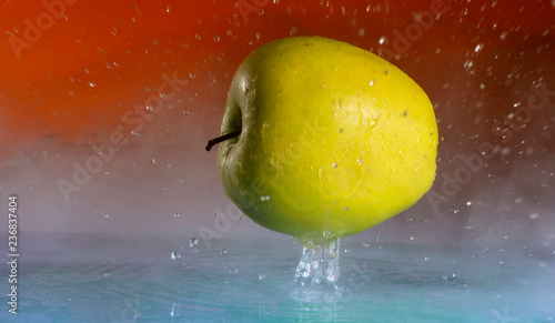 Green apple and splashes of water on a colored background