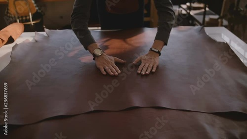 Top view male artisan spreading and touching a big piece of brown leather material in manufacturing workshop slow motion