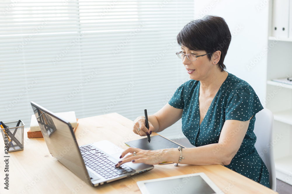 Office, graphic designer, digital - Middle age woman working at the office with laptop and digital tablet Office, graphic designer, digital - Middle age woman working at the office with laptop and digital tablet