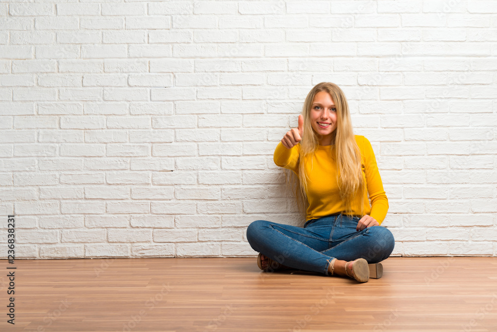 Young girl sitting on the floor giving a thumbs up gesture and smiling Young girl sitting on the floor giving a thumbs up gesture and smiling
