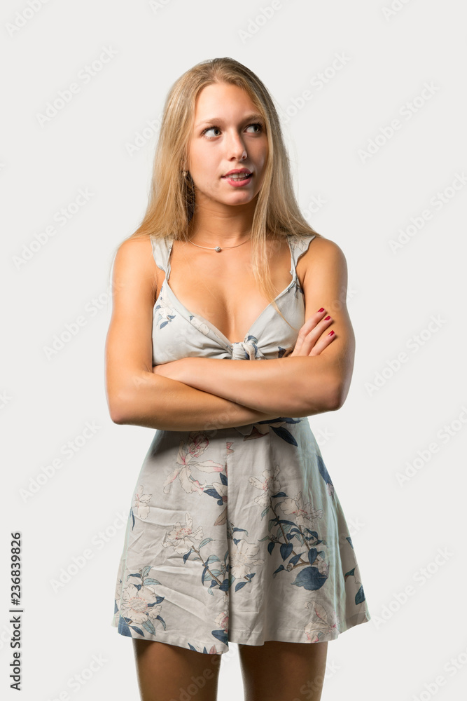 Young blonde woman having doubts and with confuse face expression while bites lip. Questioning an idea on grey background Young blonde woman having doubts and with confuse face expression while bites lip. Questioning an idea on grey background