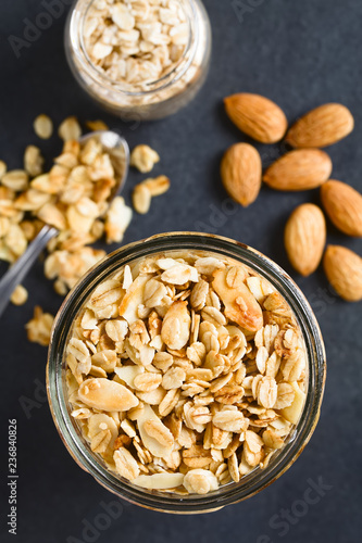 Hausgemachtes frisches Knuspermüsli aus Haferflocken, Mandeln, Honig und Kokosöl auf Schiefer fotografiert (Selektiver Fokus, Fokus auf das Müsli im Glas) photo