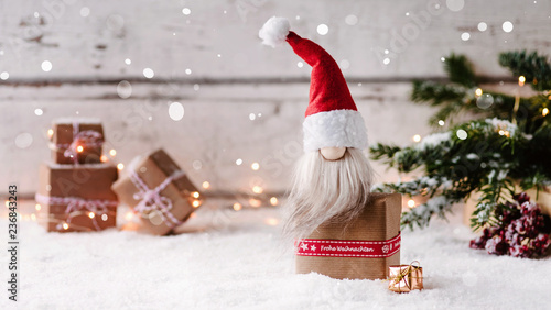 Frohe Weihnachten - Kleiner Weihnachtswichtel sitzt auf einem Geschenk und freut sich auf Heiligabend