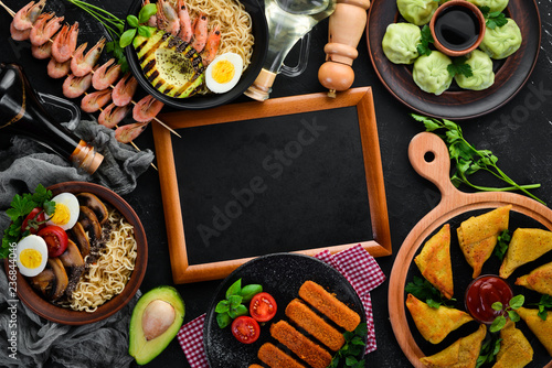 Set Asian food. Noodles, shrimp, Samsa, khinkali. On a black wooden background. Top view. Free copy space.
