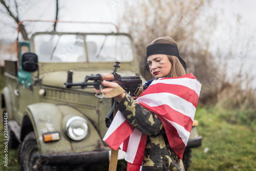 Woman with american flag and rifle near military car