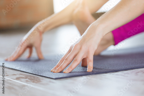 Close-up of feet and hands of attractive sporty woman practicing yoga indoor on wooden floor on fitness mat. Beautiful fitness girl doing yoga asana in loft class. Healthy lifestyle, calmness, relax