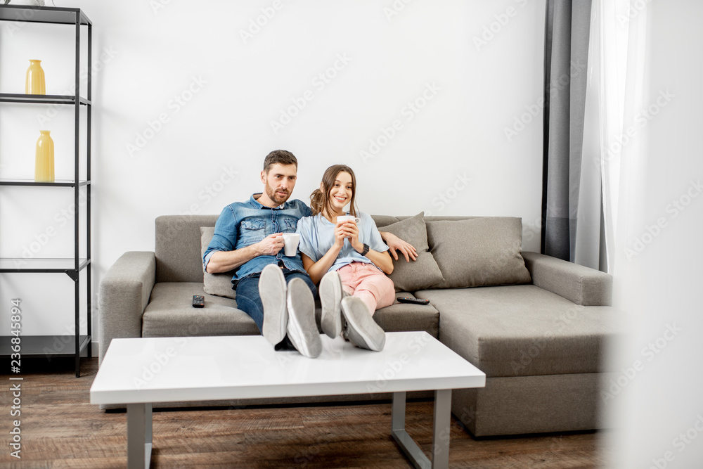Young couple dressed casually sitting together on the couch and watching TV at home. Wide interior view Young couple dressed casually sitting together on the couch and watching TV at home. Wide interior view