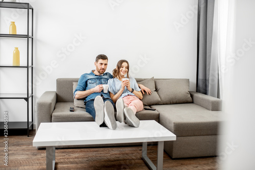 Young couple dressed casually sitting together on the couch and watching TV at home. Wide interior view