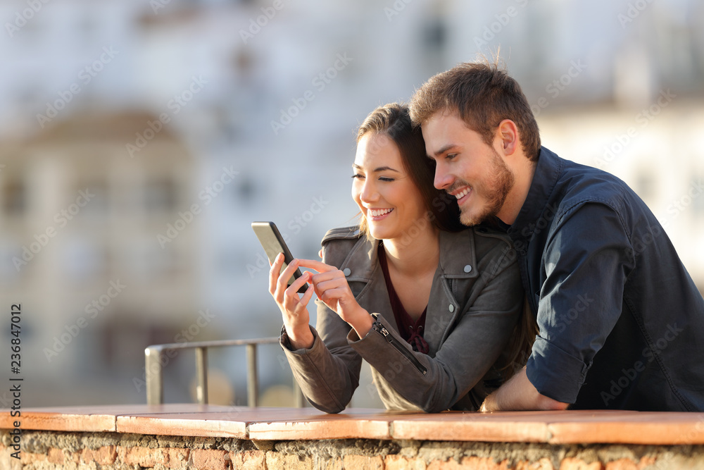 Fototapeta Szczęśliwa para używa telefon w balkonie przy zmierzchem
