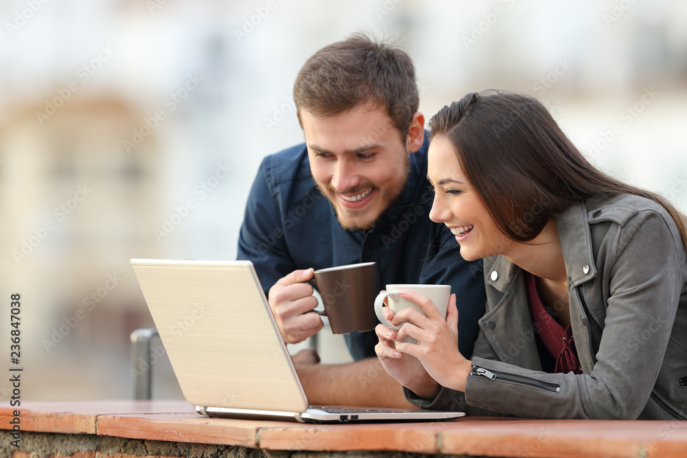 Happy couple checking laptop content on a balcony Happy couple checking laptop content on a balcony