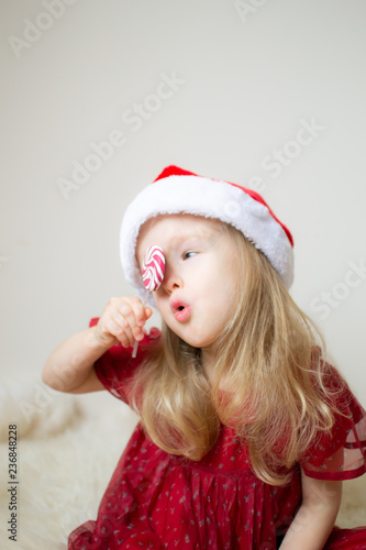 Little Beautiful Girl in Santa Hat Red Party Dress Waiting for Christmas and New Year Indoor Happy