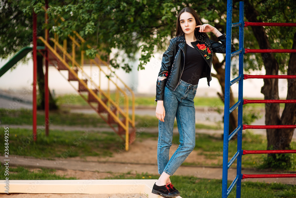 Obraz premium Portrait young punk rock fashion girl in black leather jacket with stiletto in a street warehouse urban environment, woman in jeans in the park