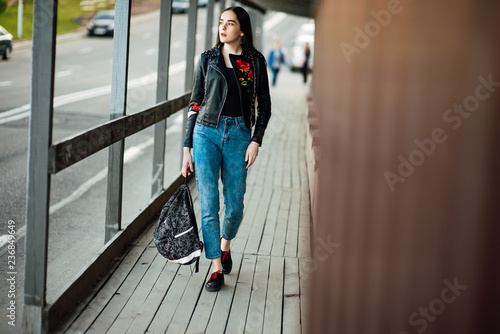 Portrait young punk rock fashion girl in a black leather jacket with stilettos in an urban environment of a street warehouse, woman in jeans walking