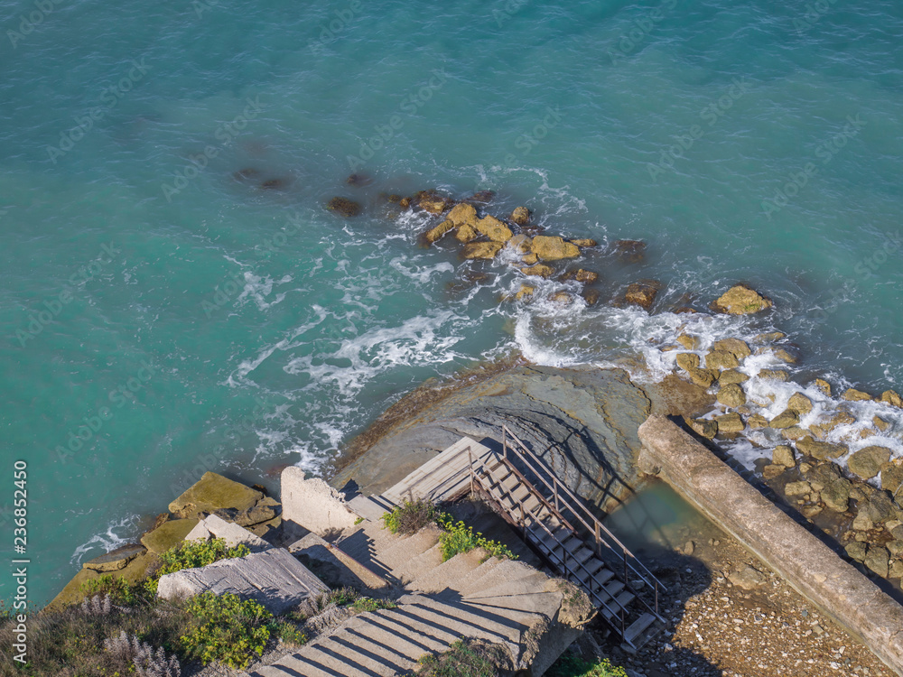 concrete steps on a steep slope leading to the rocky blue sea shore, aerial view, corfu greece