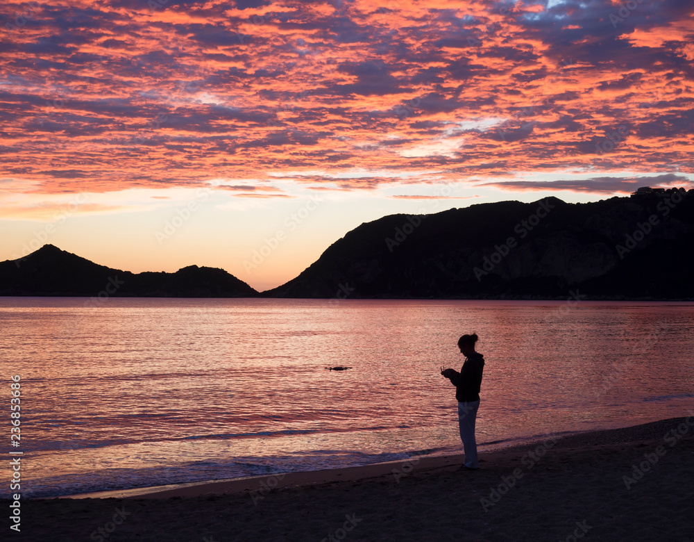 men silhoutte flying a drone during beautiful blue pink orange clouds sunset on Agios Georgios Pagon beach at Corfu island, Greece with view on porto timony bay