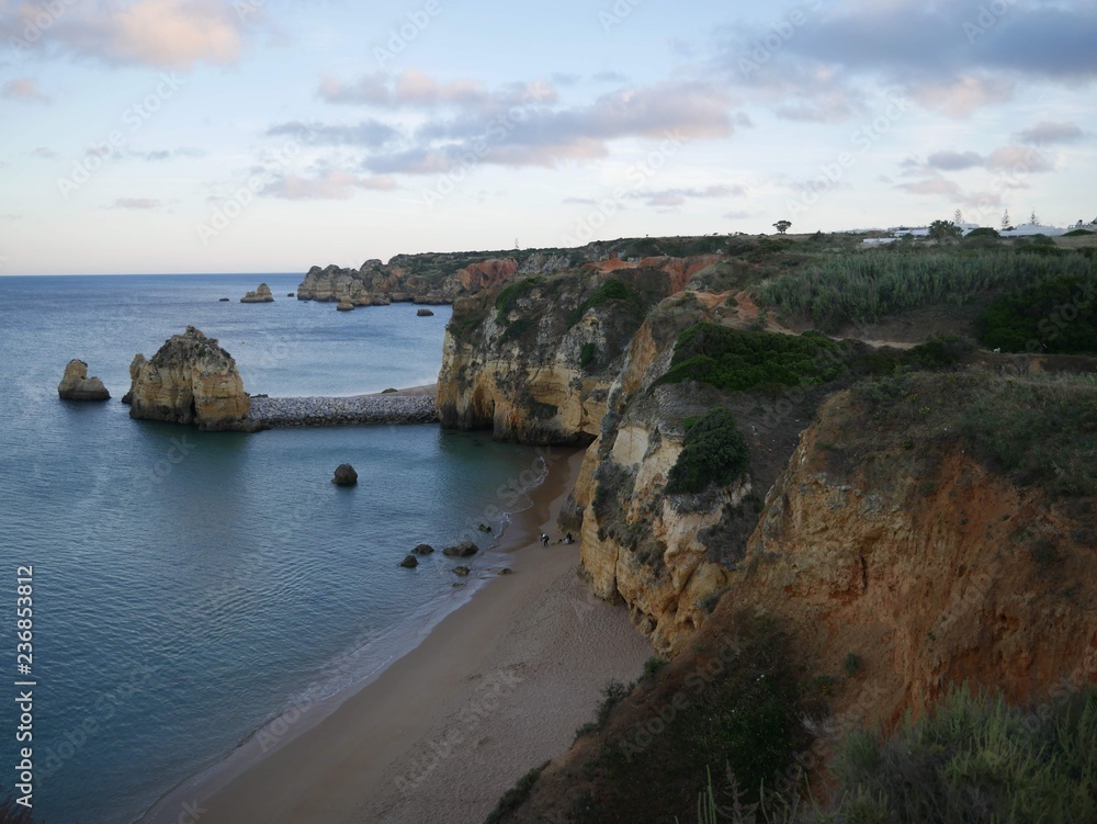 Panorama of steep cliffs next to a sandy beach and the light blue sea bathed in orange light during the sunset in Lagos, Algarve, Portugal