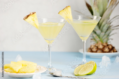 Two glasses with pineapple drink. Glasses are decorated with slices of pineapple and lime. In the background pineapple. Light background. Close-up. 