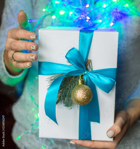 Gift with spruce branch in female hands on the background of blue bokeh garland photo