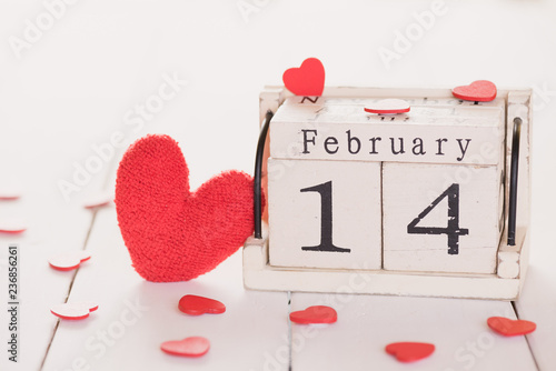 Valentines day concept. February 14 text on wooden block with handmade red heart on white wooden background.