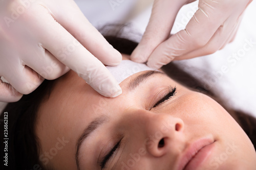 Doctor Waxing Woman's Forehead