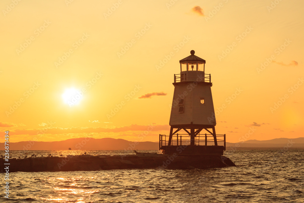 A beautiful orange sunset behind a lighthouse in front of Burlington Vermont