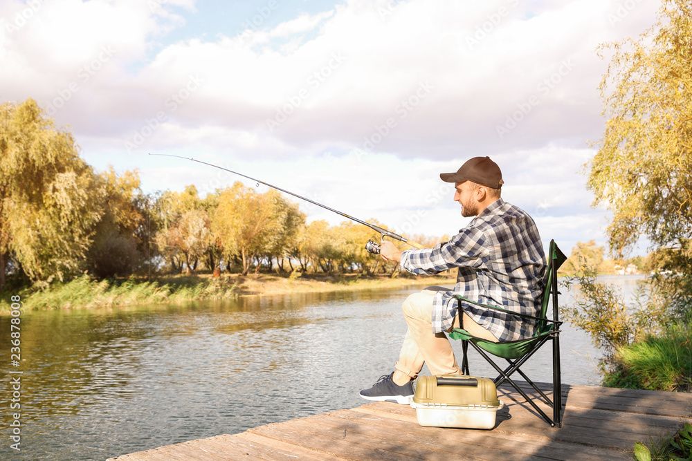 Man with rod fishing on wooden pier at riverside. Recreational activity Man with rod fishing on wooden pier at riverside. Recreational activity