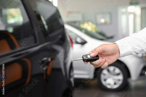 Young man turning off alarm system with car key indoors, closeup