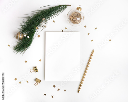 Christmas composition in gold. Paper blank mock up, christmas fir tree branch with glass ball decorations, star confetti, pen on white background. New year flat lay, top view, copy space, square