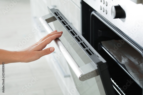 Young woman opening electric oven in kitchen, closeup