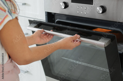 Young woman opening electric oven in kitchen, closeup