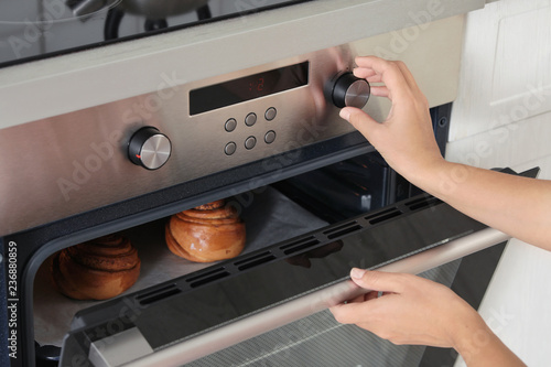 Young woman baking buns in electric oven, closeup