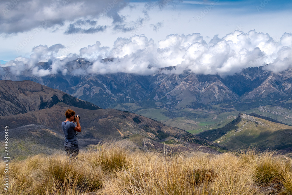 A hiker takes photos of the landscape from the top of a hill in Canterbury, New Zealand