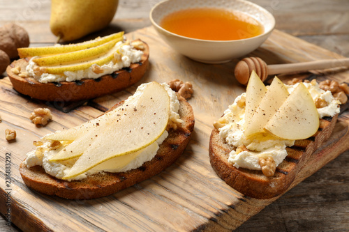 Toasted bread with tasty cream cheese and pear on wooden board