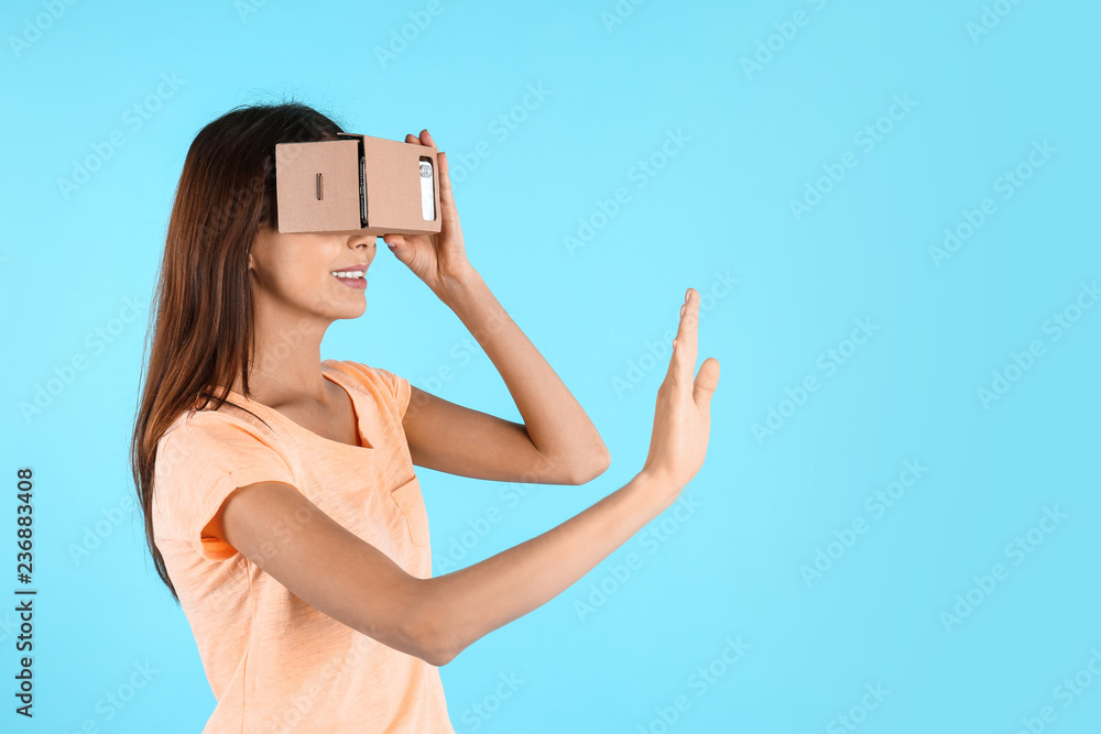 Young woman using cardboard virtual reality headset on color background. Space for text Young woman using cardboard virtual reality headset on color background. Space for text