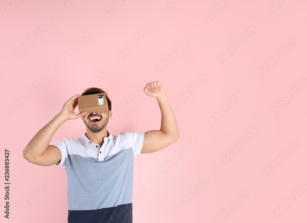 Young man using cardboard virtual reality headset on color background. Space for text Young man using cardboard virtual reality headset on color background. Space for text
