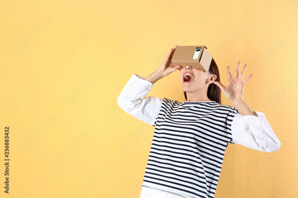 Young woman using cardboard virtual reality headset on color background. Space for text Young woman using cardboard virtual reality headset on color background. Space for text
