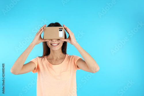 Young woman using cardboard virtual reality headset on color background. Space for text © New Africa