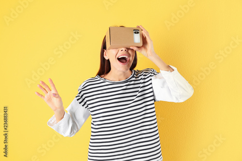Young woman using cardboard virtual reality headset on color background