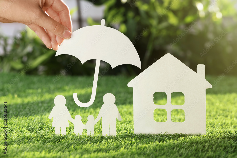 Φωτογραφία Woman holding paper umbrella over cutout of family and house on fresh grass, closeup