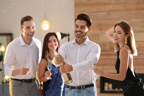 Man opening bottle of champagne among friends at party indoors