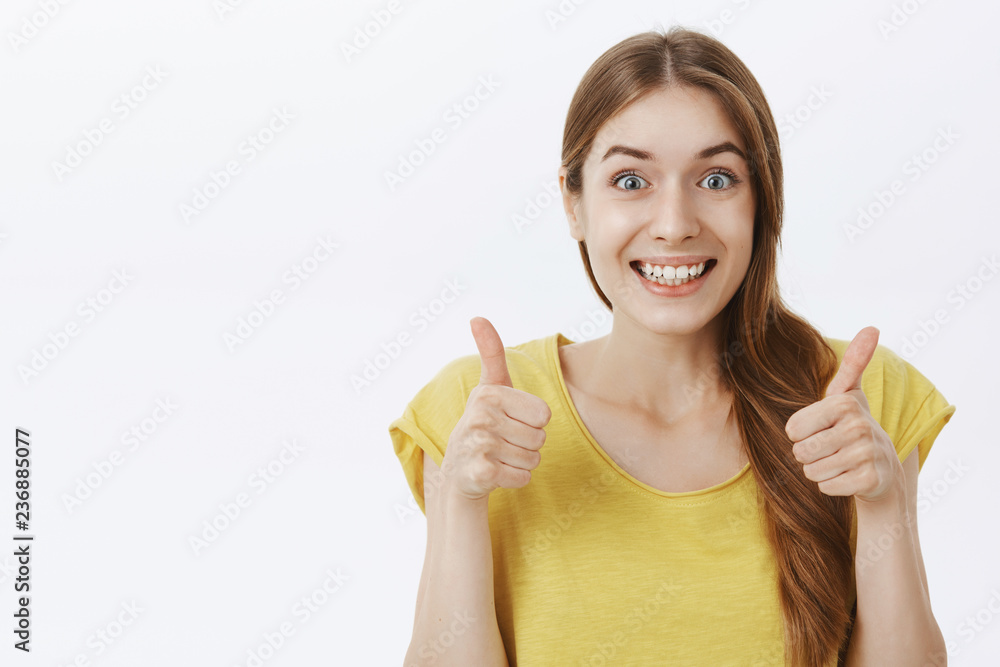 Portrait of charming excited and supportive friendly young girl with braid in yellow casual t-shirt showing thumbs up and smiling with agreement, liking idea approving good plan over gray background Portrait of charming excited and supportive friendly young girl with braid in yellow casual t-shirt showing thumbs up and smiling with agreement, liking idea approving good plan over gray background