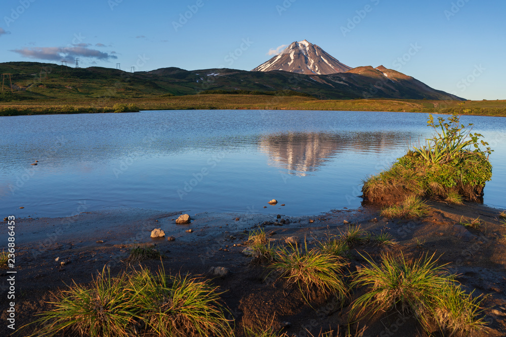 Stunning evening autumn volcanic landscape of Kamchatka Peninsula at sunset: scenery view of cone Vilyuchinsky Volcano, mountain tourist camping and reflection of mountains in beautiful alpine lake. Stunning evening autumn volcanic landscape of Kamchatka Peninsula at sunset: scenery view of cone Vilyuchinsky Volcano, mountain tourist camping and reflection of mountains in beautiful alpine lake.