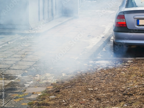 A large cloud of gray smoke from the exhaust pipe of a car in the courtyard of a residential building, ecology, urban smog, air pollution concept, horizontal frame