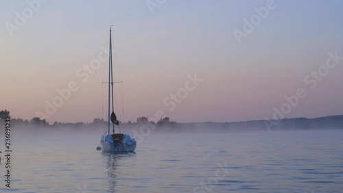 Sailboat docked on foggy lake at sunrise