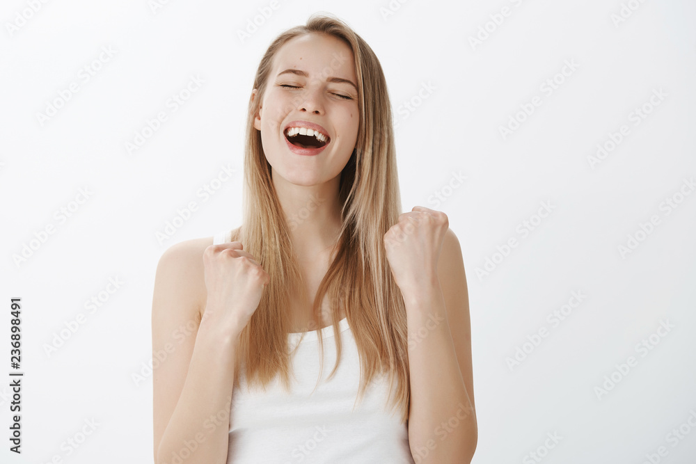 Fototapeta premium Sweet taste of success. Happy delighted and relived young woman screaming yes from victory and pleasure receiving award clenching raised fists in victory and triumoh closing eyes from satisfaction