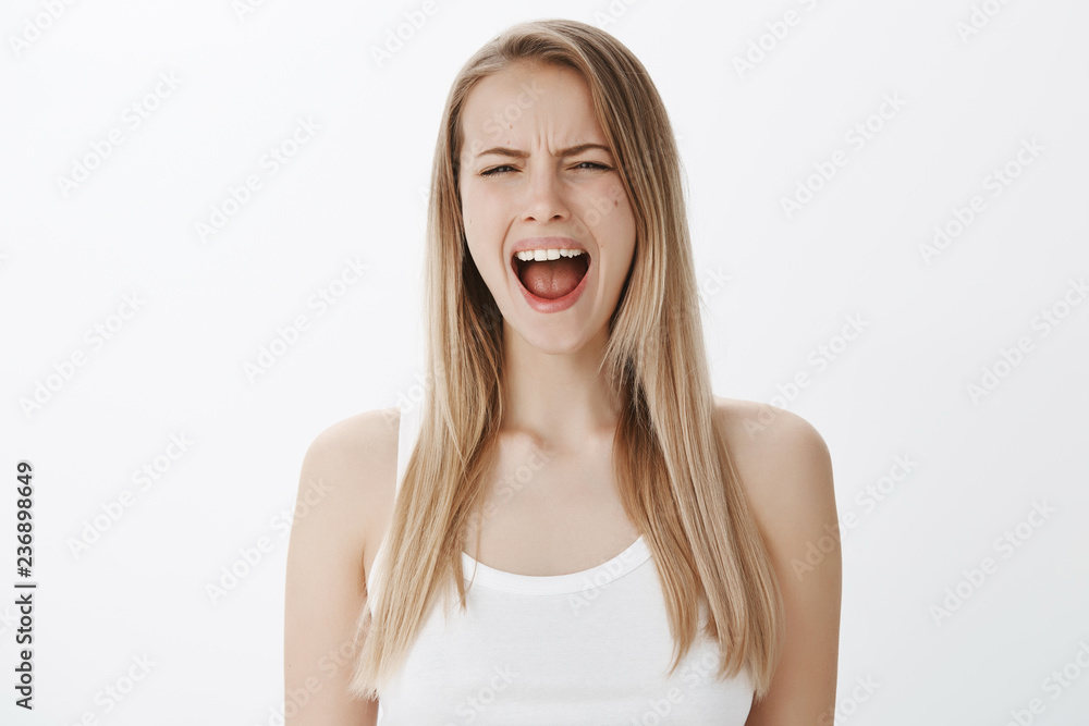 Studio shot of complaining and whining silly immature woman with blond hair crying and screaming as being displeased and offended acting like child standing displeased against gray background Studio shot of complaining and whining silly immature woman with blond hair crying and screaming as being displeased and offended acting like child standing displeased against gray background