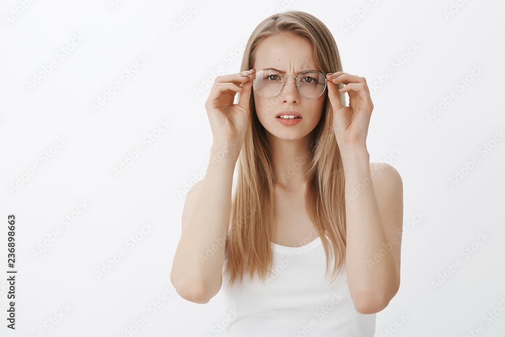 Girl cannot read sign putting on glasses squinting and frowning as looking focused at camera, trying understand what written having problems with sight standing clueless and intense over gray wall Girl cannot read sign putting on glasses squinting and frowning as looking focused at camera, trying understand what written having problems with sight standing clueless and intense over gray wall