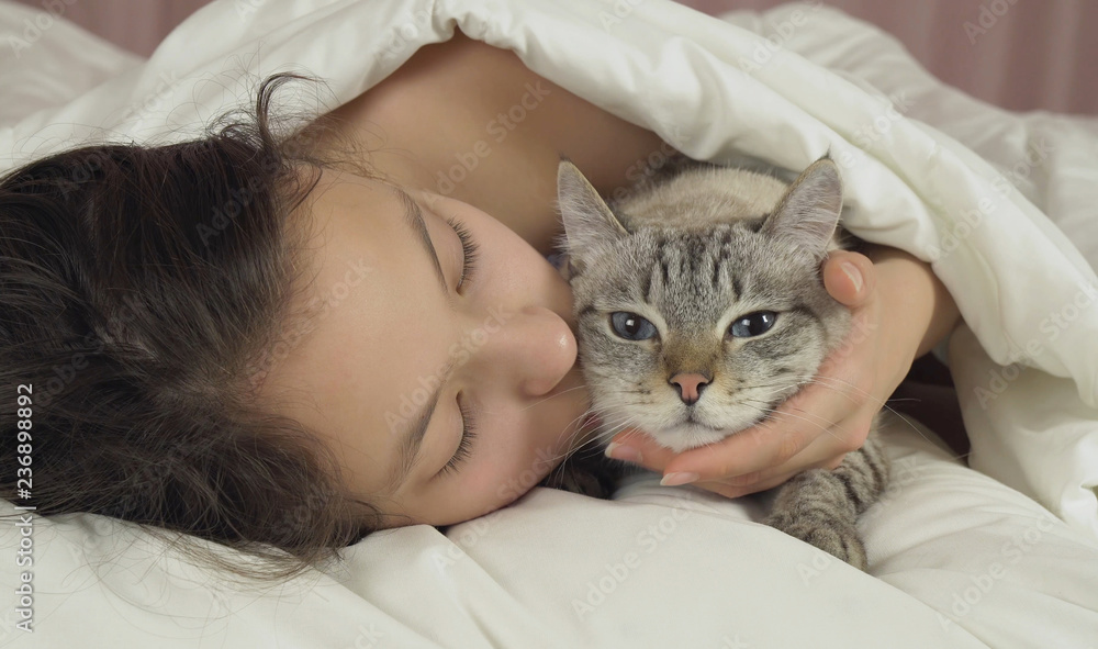 Happy teen girl kisses and talks with Thai cat in bed